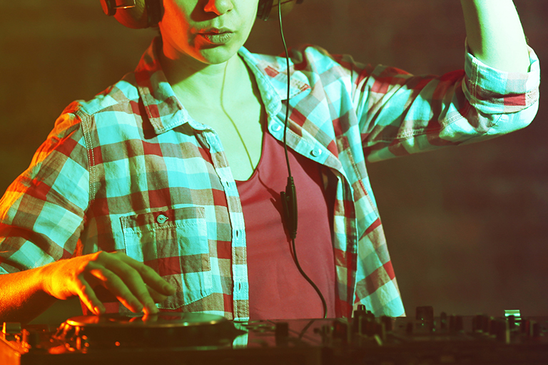 a female EDM artist using a mixer under dim club lighting 