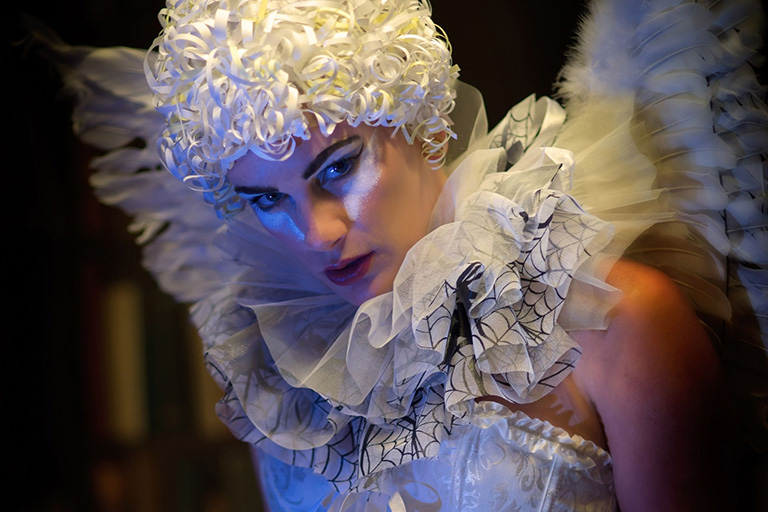 A Cirque Du Soleil performer wearing a white wig, angel wings, and an organza collar 