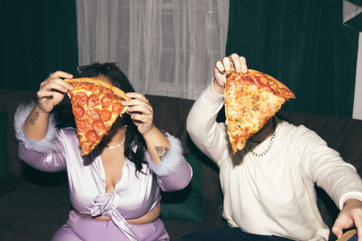 two people at a party holding up pizzas the size of their faces