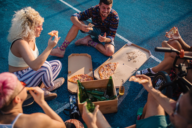 a group of friends eat pizza and drink beer outside