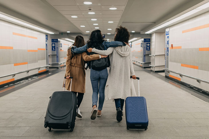Three women with suitcases walk down an airport hallway